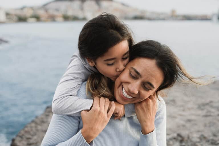 Daughter kissing her mom with sea in the background